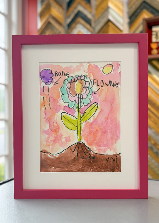 Custom framed children’s artwork of a colorful flower with labeled parts, displayed in a bright pink frame with white matting