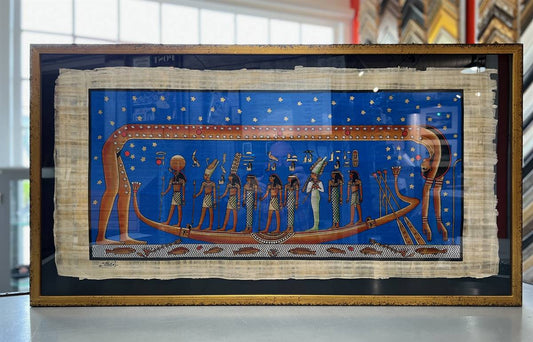 Hand-painted Egyptian papyrus framed in AMCI gold with black mat and Conservation Glass, showcasing vivid blue and gold tones.