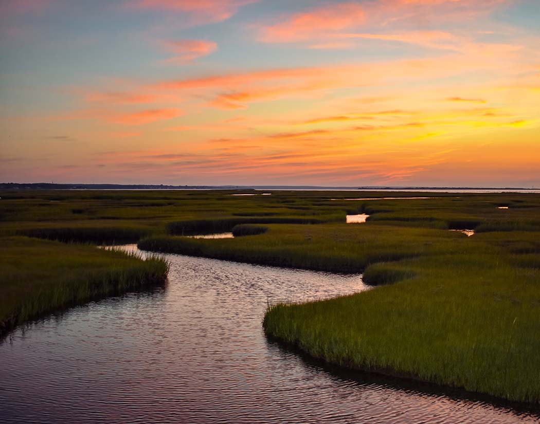 Sunset over a marsh with winding waterways and grasslands.