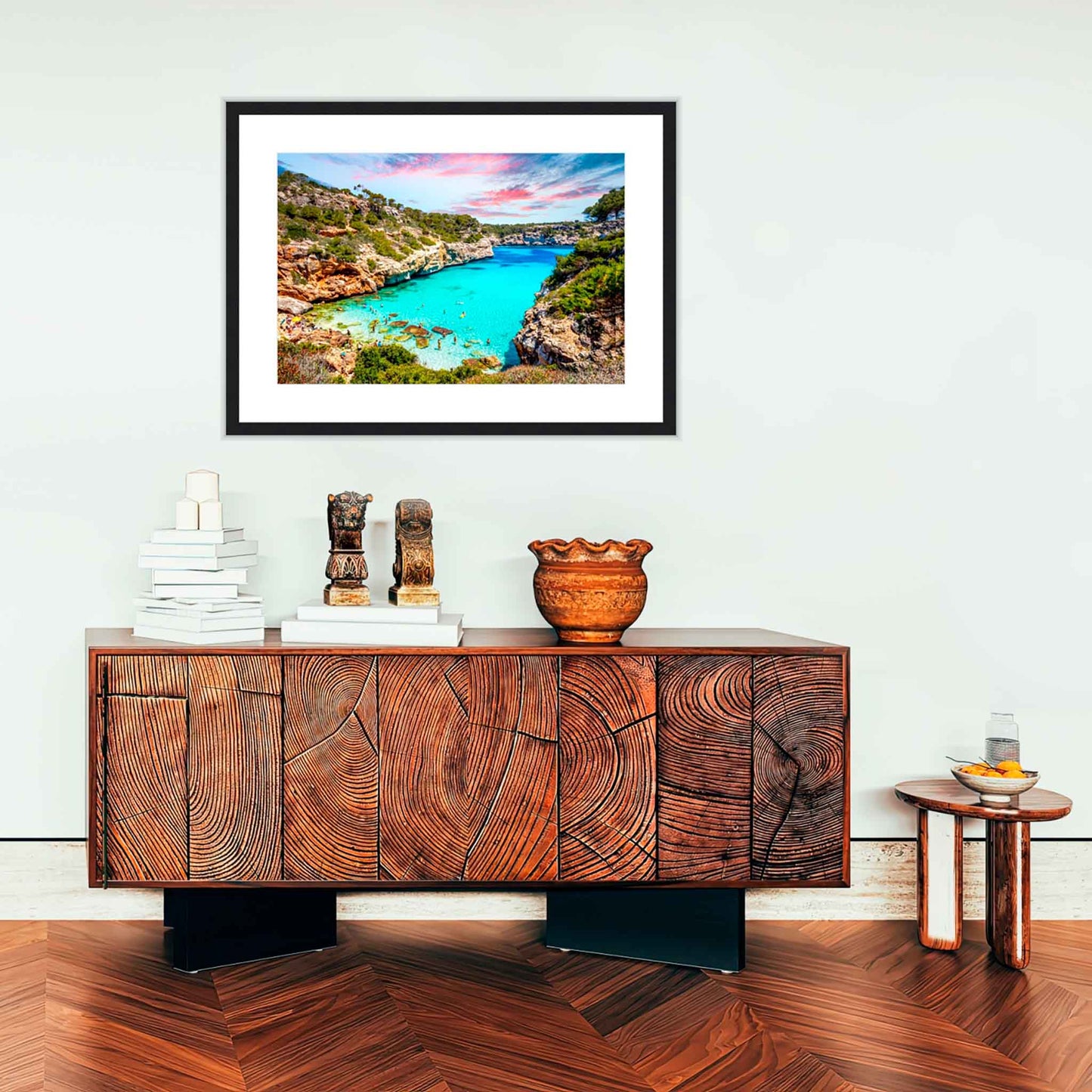 Wooden sideboard with decorative items in a room with a framed photograph of a scenic landscape on the wall.