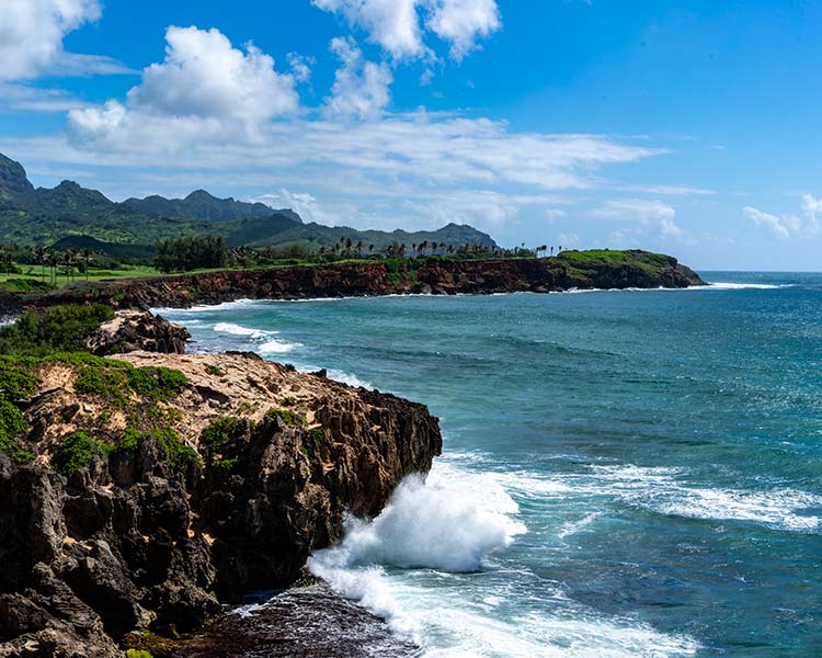 Coastal landscape with rocky cliffs and ocean waves, under a blue sky with clouds.