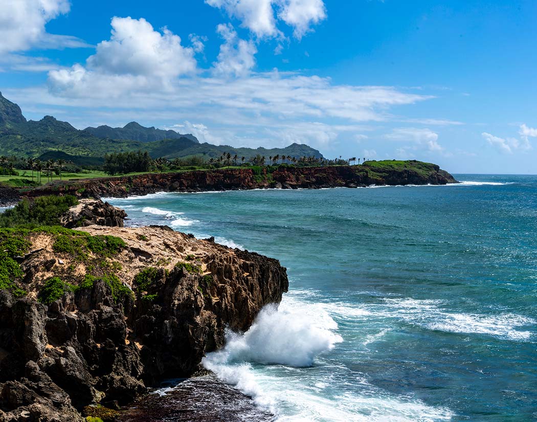 Coastal landscape with rocky cliffs and ocean waves, under a blue sky with clouds.