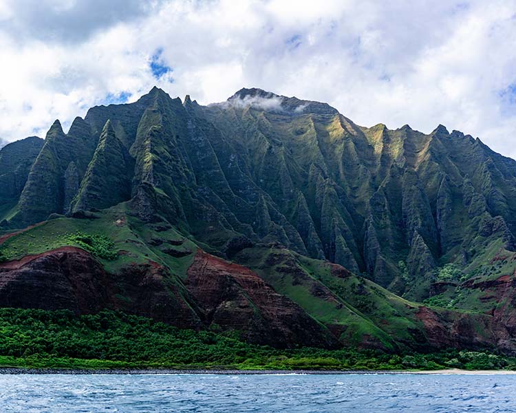 Mountain range with lush greenery and a body of water in the foreground