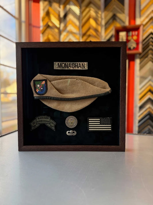 Army Ranger beret and uniform patches arranged in a dark wood shadowbox with black background.