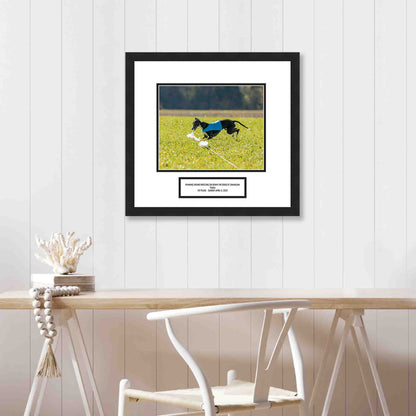 Framed picture of a dog running on grass with a white wall and table in the background