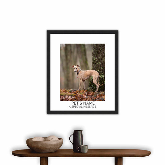 Framed picture of a dog in a forest on a wall above a wooden console table.